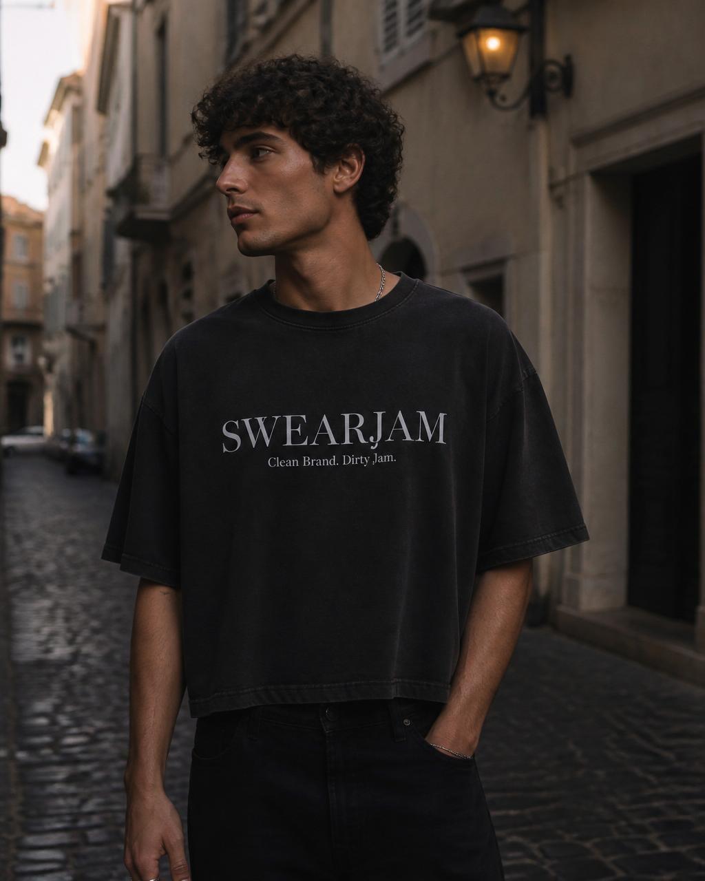 Swearjam — chalk-white SWEARJAM wordmark on a washed black tee, photographed on a cobbled street