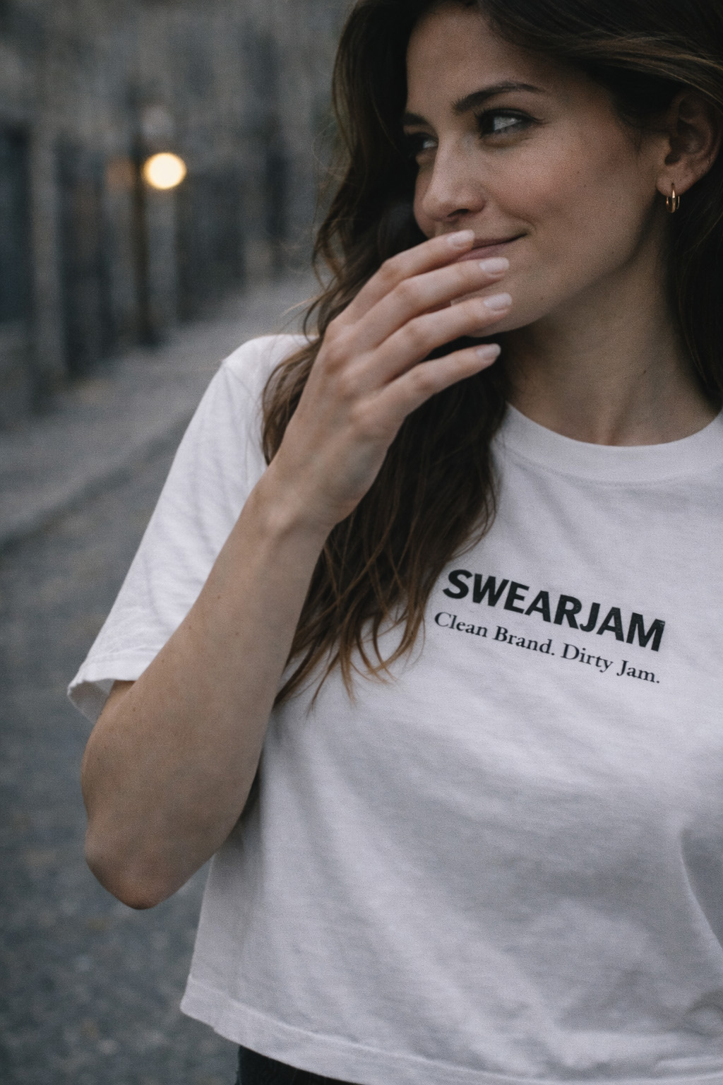 Swearjam cropped white tee with SWEARJAM wordmark and 'Clean Brand. Dirty Jam.' tagline, photographed on a cobbled street